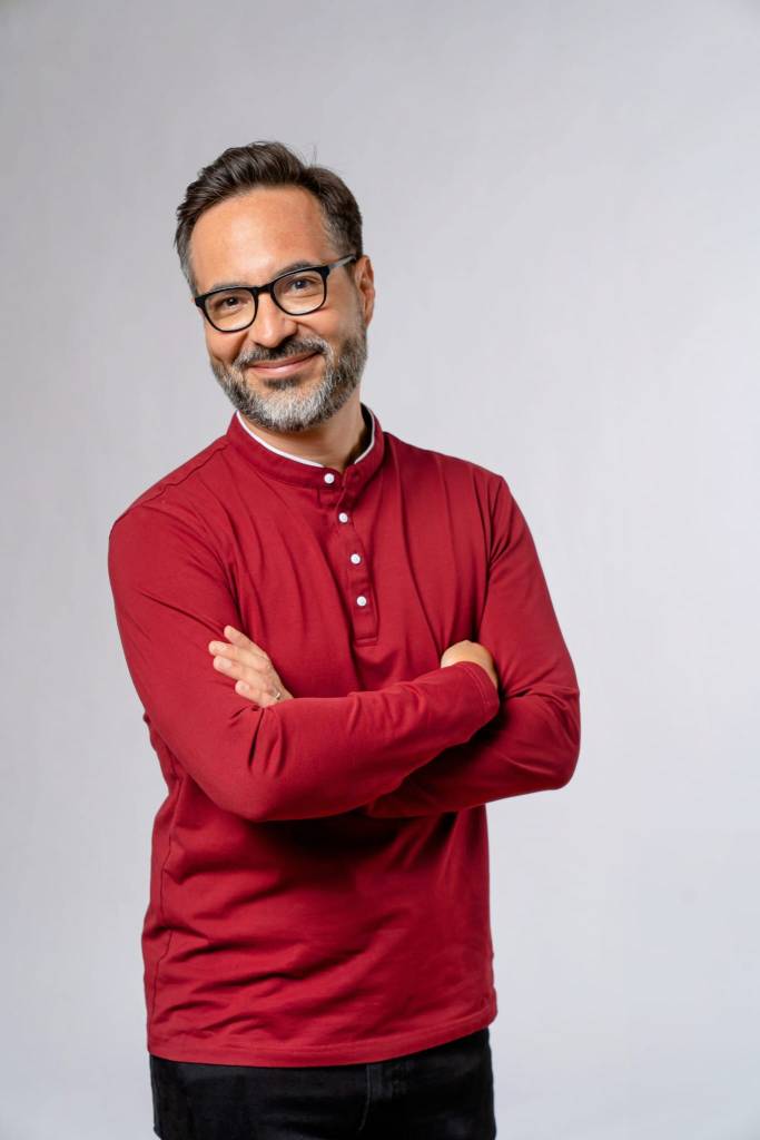 The author, David Cuen, wears a red shirt, has his arms crossed and is looking at the camera