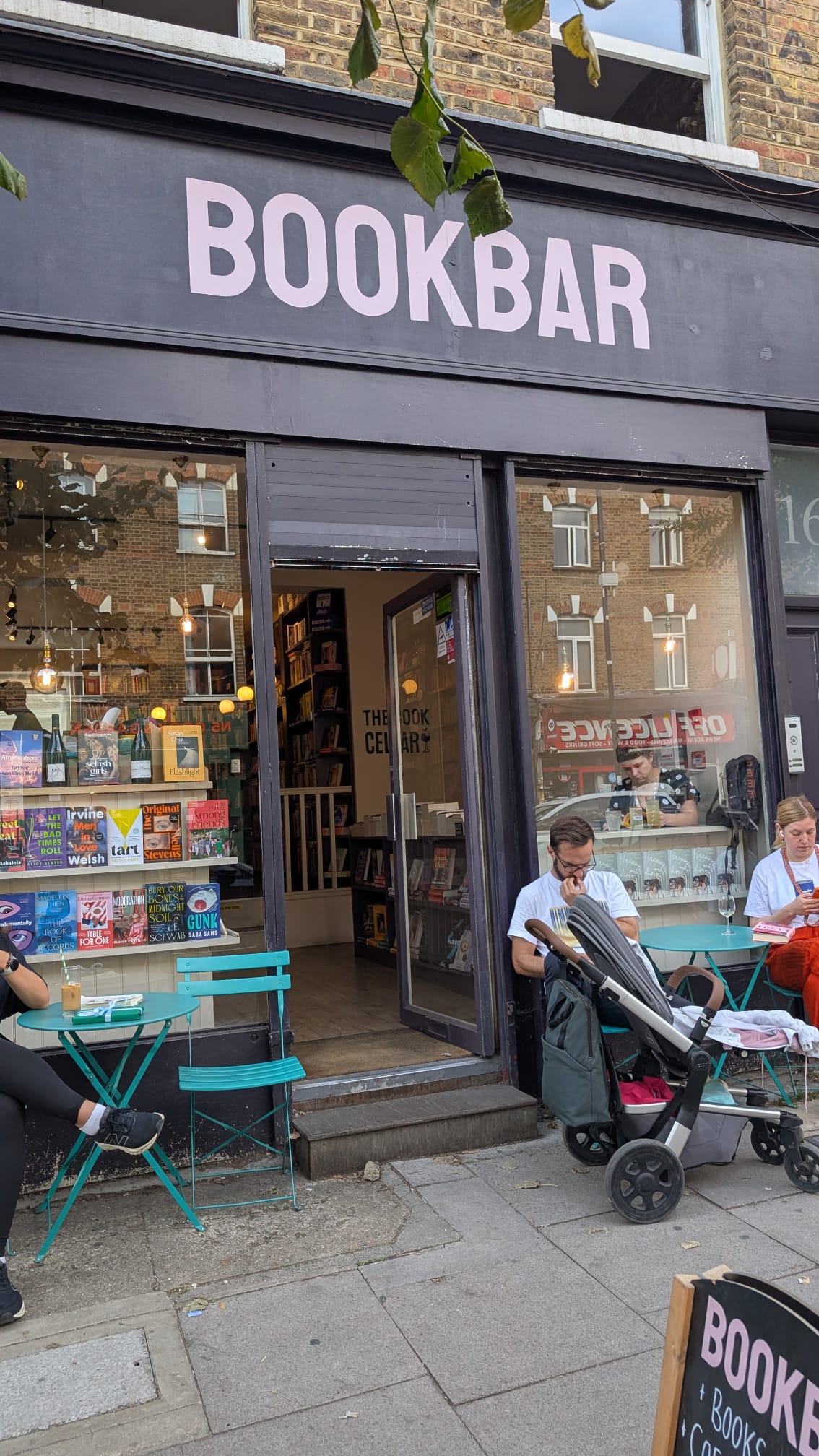 Image of the exterior of BookBat with pink letters in Islington. People are reading outside